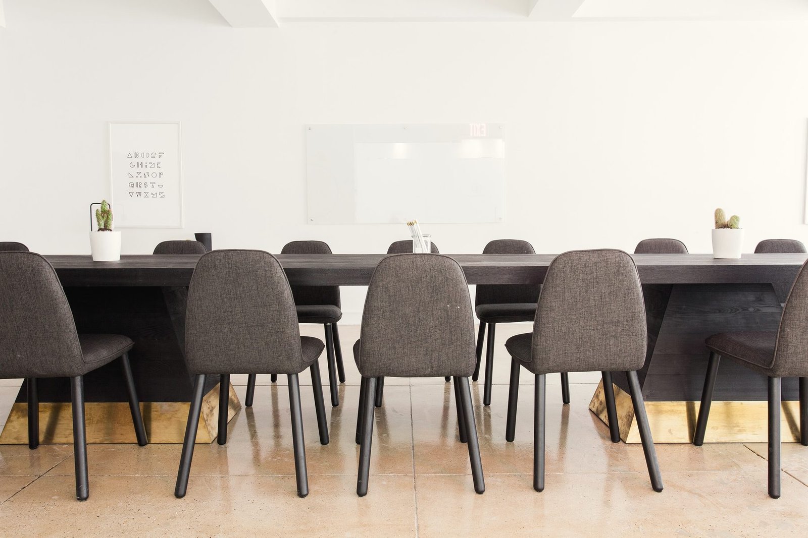A long dark conference table lined with grey upholstered chairs in a bright room