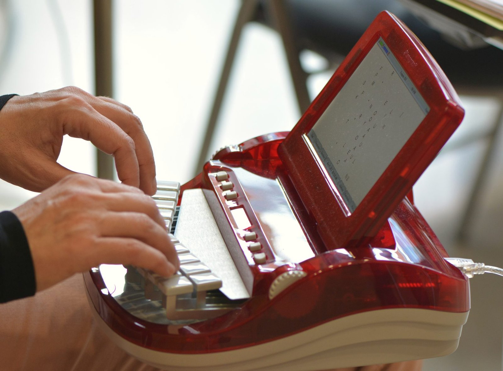 Hands on the keys of a red stenographic writer with a tilted screen