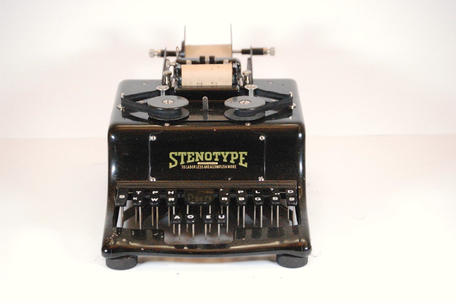 An early black Stenotype machine with a paper roll on top, photographed on white
